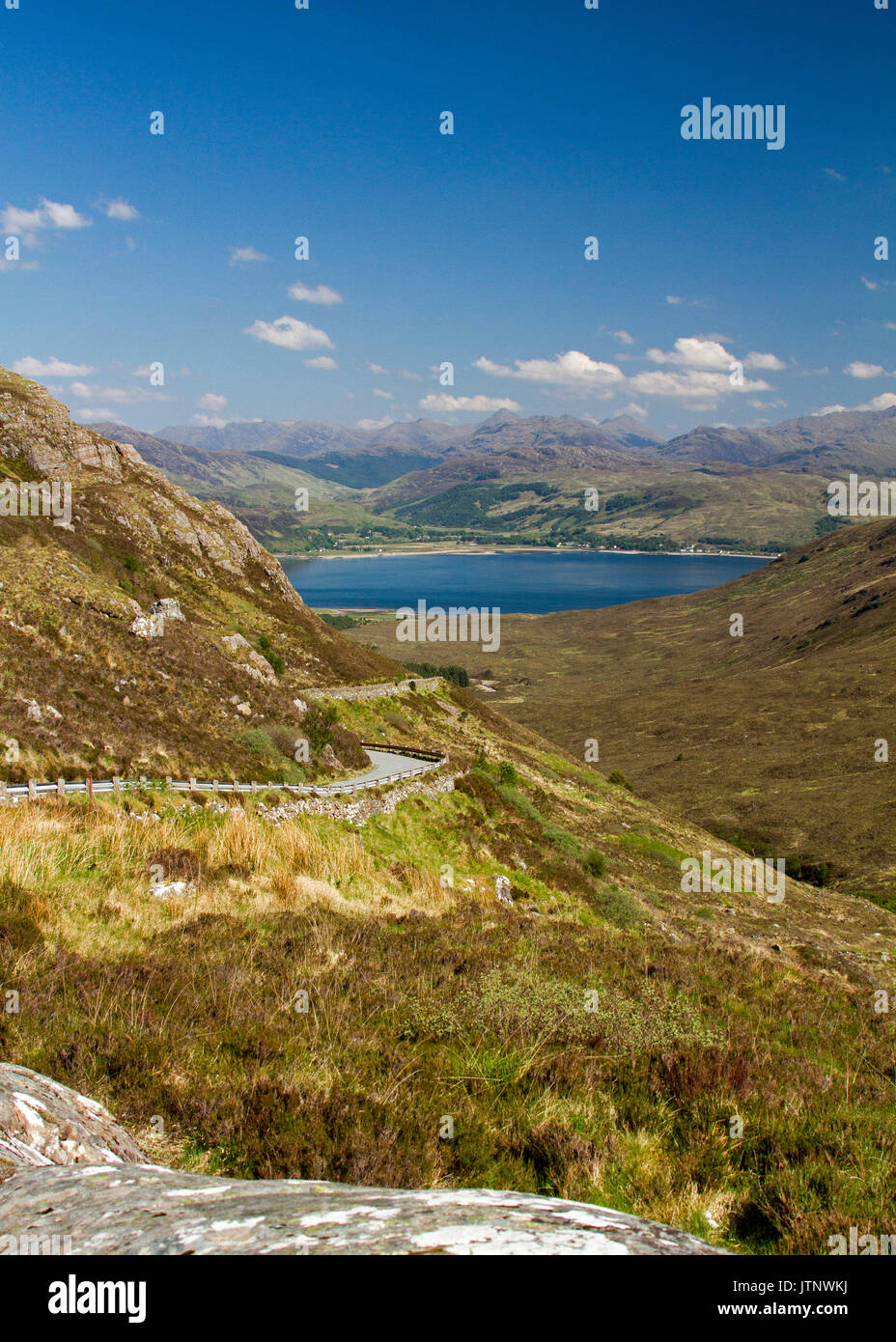 Spettacolare vista lungo la strada per Kylerhea sull isola di Skye, con montagne di terraferma scozzese di distanza al di là di acque blu dell'oceano sotto il cielo blu Foto Stock