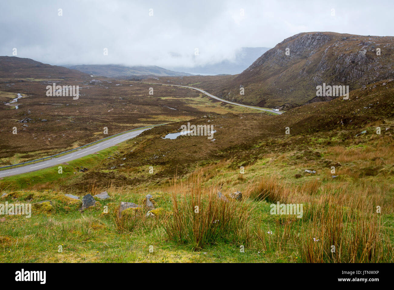 Strada stretta mediante avvolgimento e vasto altopiano montuoso paesaggio con bassa e nebbioso nuvole vicino: Achmelvich, Scozia Foto Stock