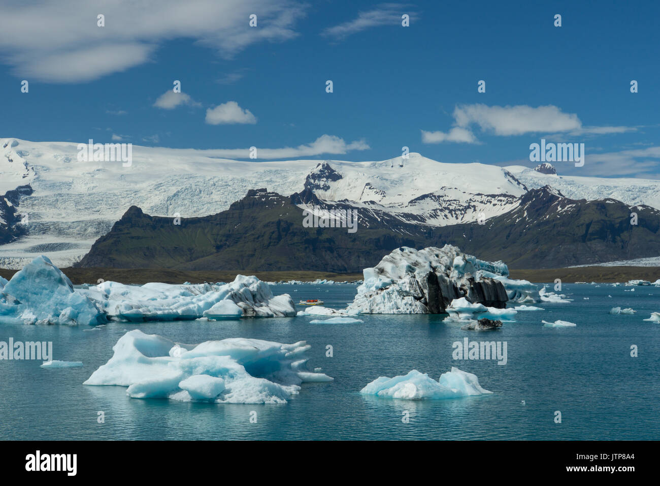 Islanda - Giant ice floes con la barca tra il ghiacciaio e le montagne sullo sfondo Foto Stock