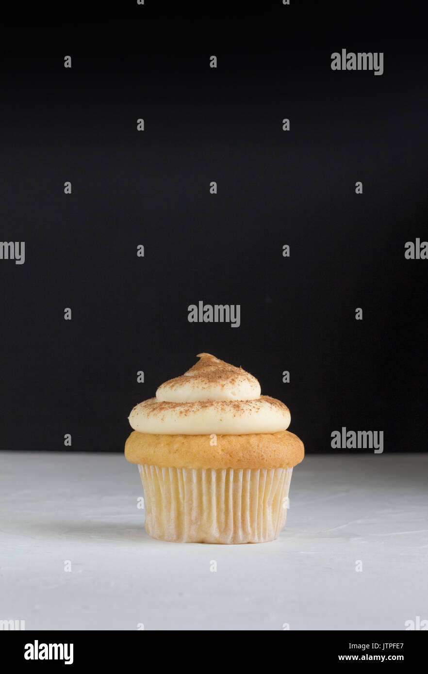 Cup cake sfondo con singola tortina su bianco e rabboccato con cannella crema pasticcera sul bianco rustico con sfocati sullo sfondo nero - spazio per il testo Foto Stock