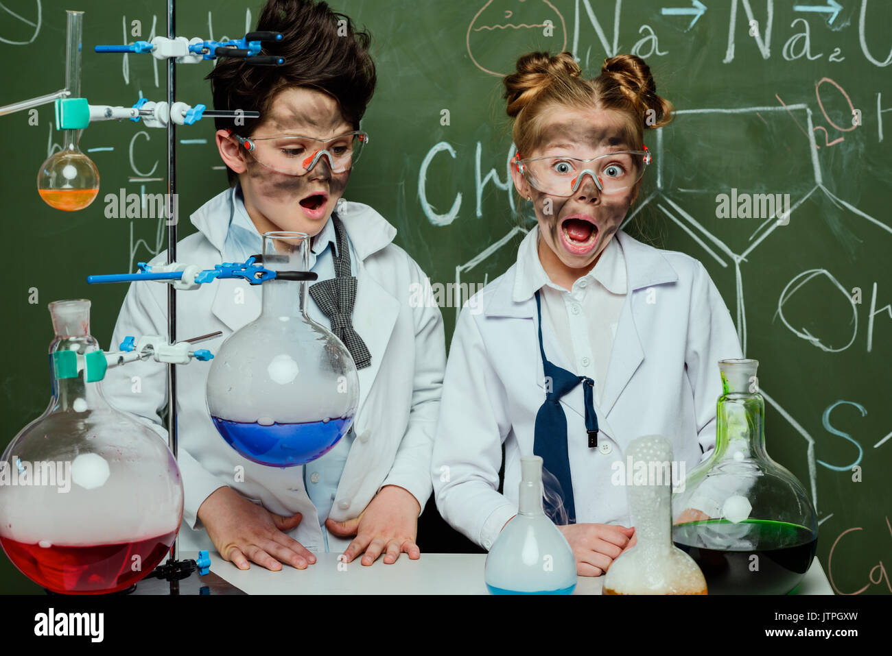 Bambini piccoli in camici con lavagna dietro in Science Laboratory, scienziati kids concetto del team Foto Stock