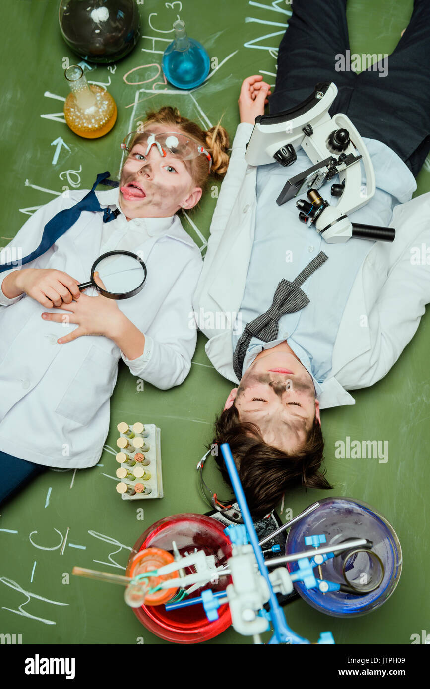 Vista in elevazione dei ragazzi in camice da laboratorio giacente sulla lavagna dopo l'esperimento, gli scienziati kids concetto del team Foto Stock