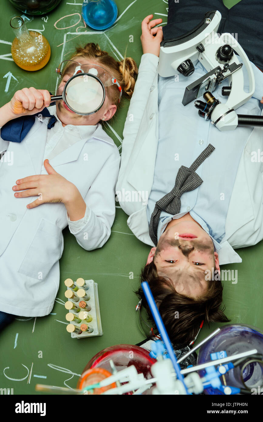 Vista in elevazione dei ragazzi in camice da laboratorio giacente sulla lavagna dopo l'esperimento, gli scienziati kids concetto del team Foto Stock