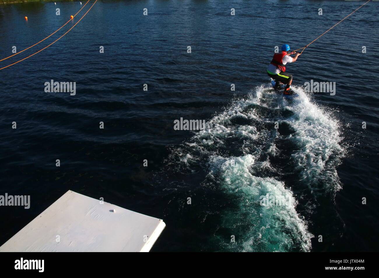 Giovane uomo di essere lanciato tirato dal cavo sul Wakeboard nel lago Foto Stock