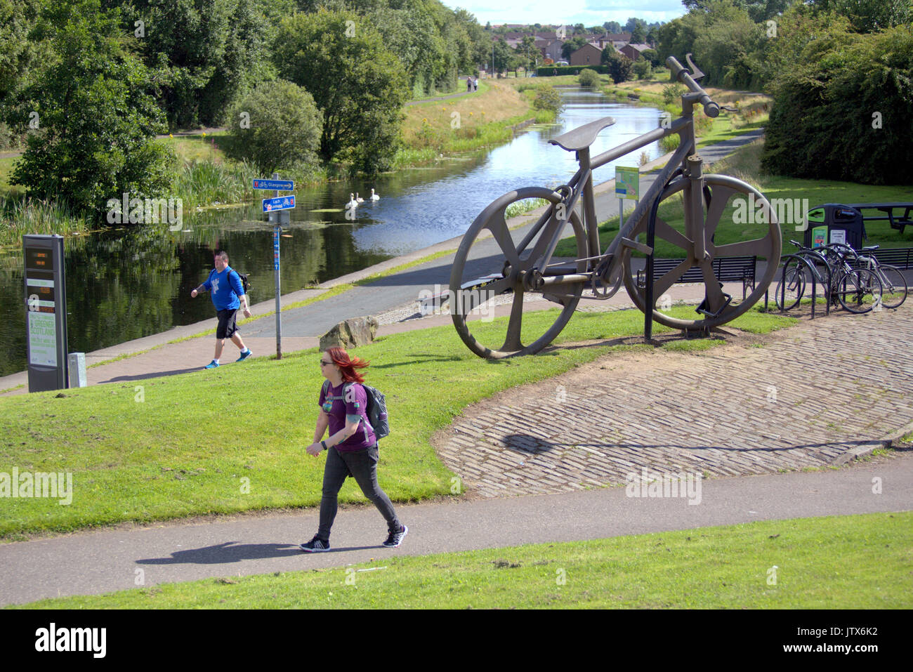 La gente del posto a piedi NCN 7 passa la bici Bankies scultura a Clydebank Estate meteo locali e godetevi l'estate sul canale di Forth e Clyde alzaia Foto Stock