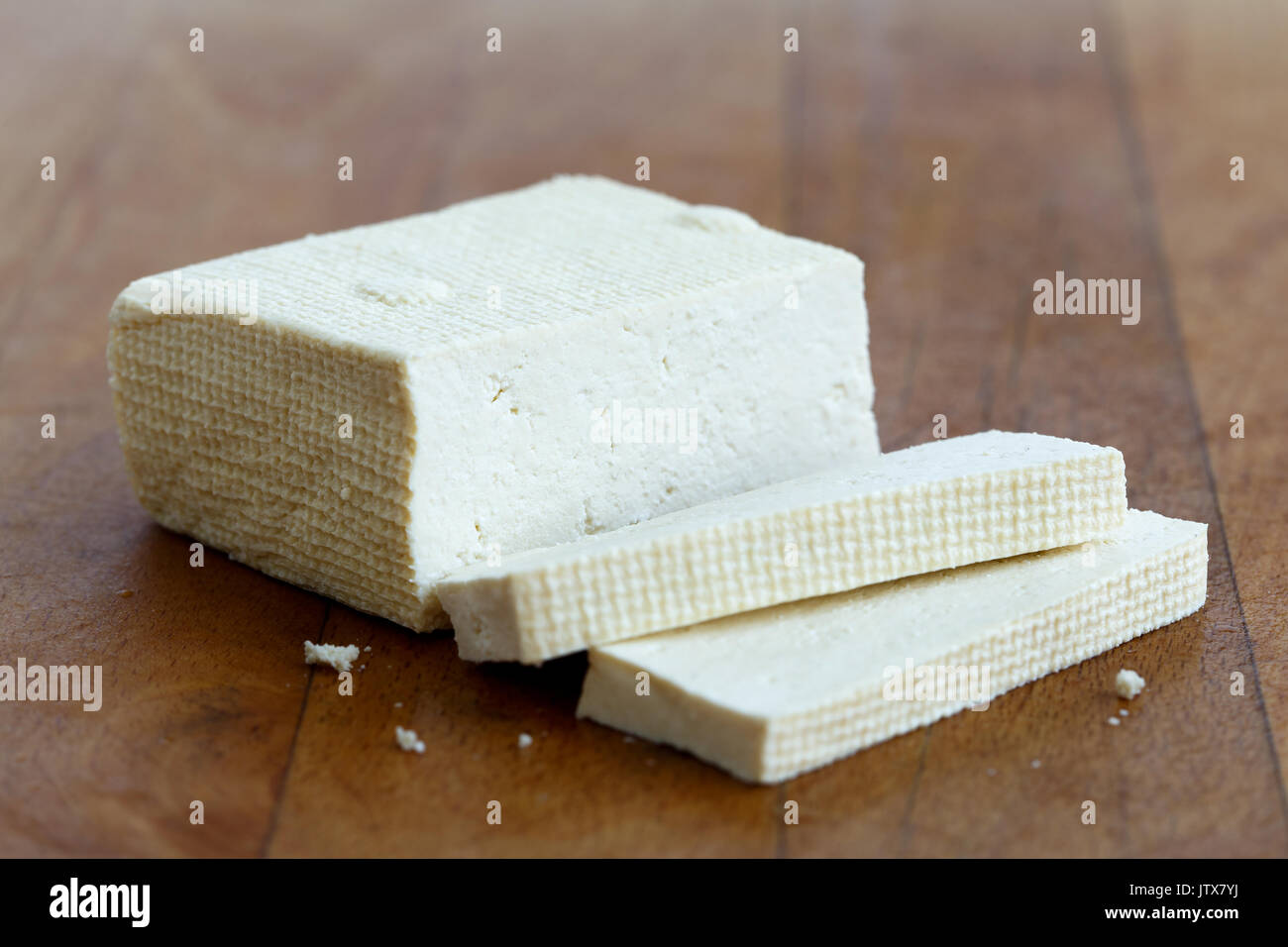 Blocco di tofu bianco e due fette di tofu sul tagliere di legno. Foto Stock