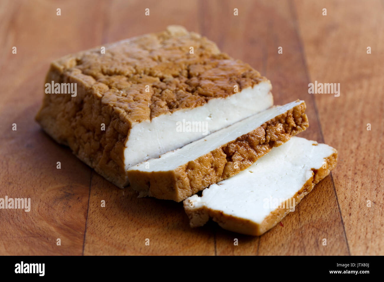 Blocco di tofu affumicato e due fette di tofu sul tagliere di legno. Foto Stock