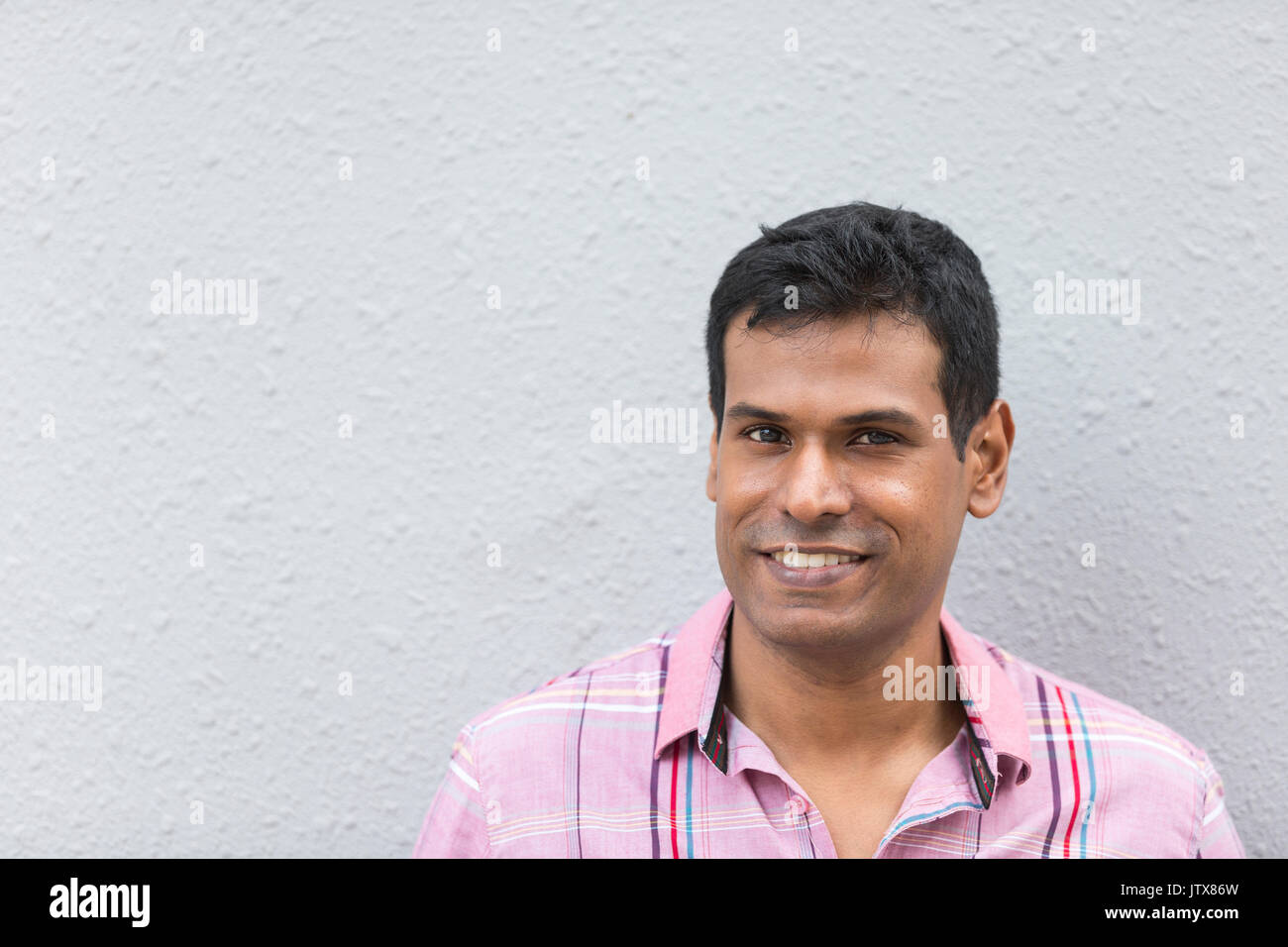 Indian uomo appoggiato su di un muro grigio. Bel giovane uomo asiatico appoggiata contro un muro grigio e guardando la telecamera Foto Stock