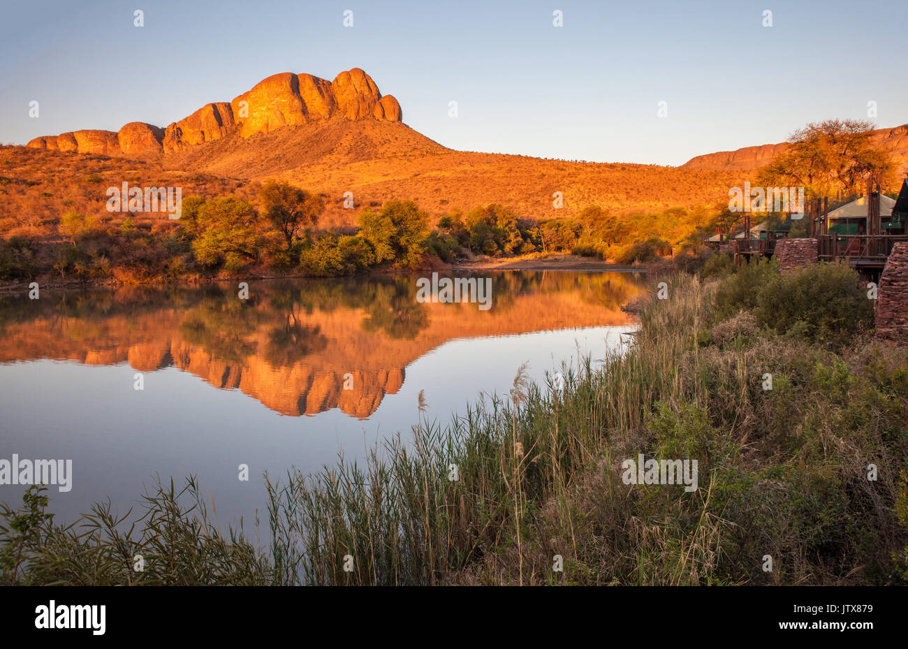 Tlopi Tented Camp che si affaccia su piazza Dam con il Waterberg montagne riflessa nell'acqua ancora al tramonto in Marakele National Park, Provincia di Limpopo Foto Stock