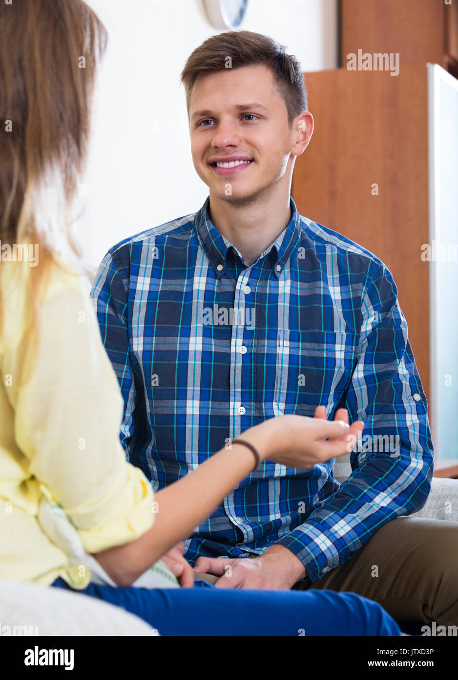 Sorridente giovane ragazzo avente la conversazione positiva con la sua fidanzata in ambienti interni Foto Stock