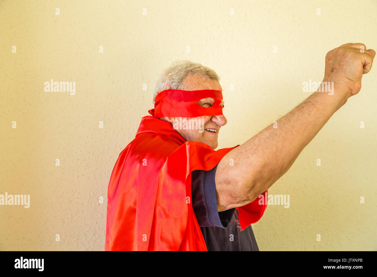 Il vecchio uomo vestito da supereroe pugno di sollevamento che mostrano la potenza Foto Stock