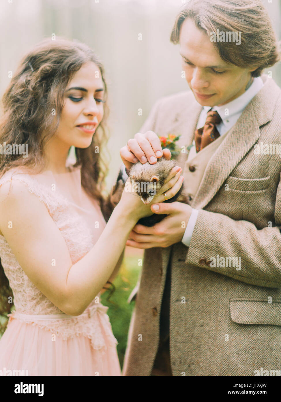 Close-up foto della Sposa sorridente tenendo il marrone ferret mentre il vintage vestito sposo petting è l'animale. La composizione della foresta. Foto Stock