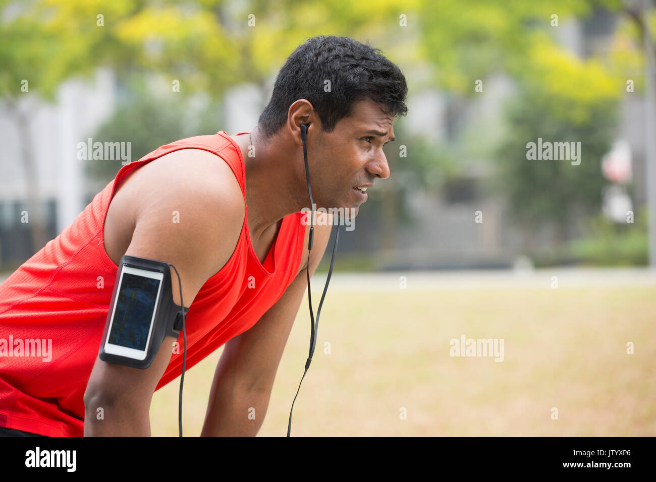 Ritratto di atletica uomo indiano riposando dopo aver percorso urbano attraverso le strade delle città. Maschio asiatici runner prendendo pausa rilassante permanente. Foto Stock