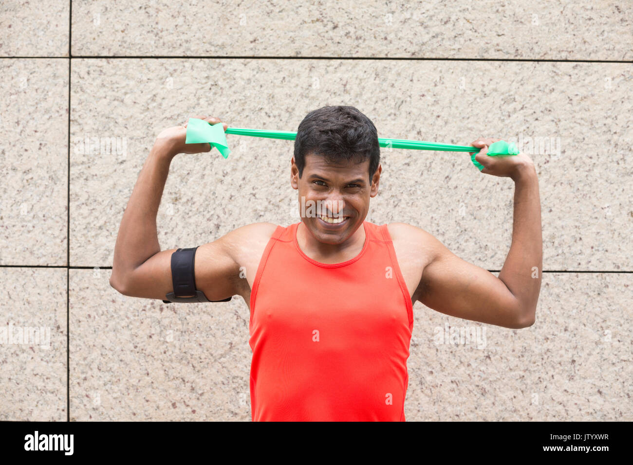 Ritratto di un atletico uomo indiano utilizzando bande di stiramento all'aperto nel contesto urbano. Foto Stock