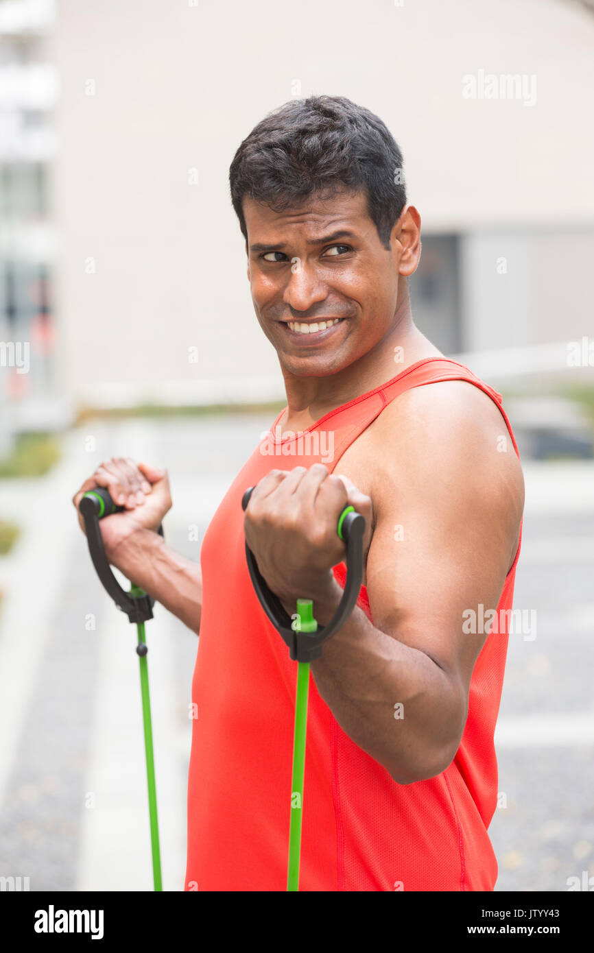 Ritratto di un atletico uomo indiano utilizzando bande di stiramento all'aperto nel contesto urbano. Foto Stock
