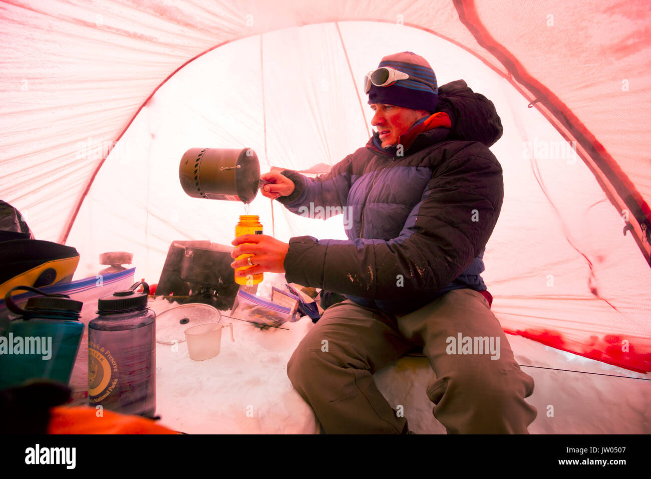 Un alpinista è neve di fusione per ottenere acqua potabile, all'interno di una tenda ad alta Camp sul Denali in Alaska. La mattina presto stanno andando per un vertice a spingere per la montagna più alta del Nord America. Foto Stock