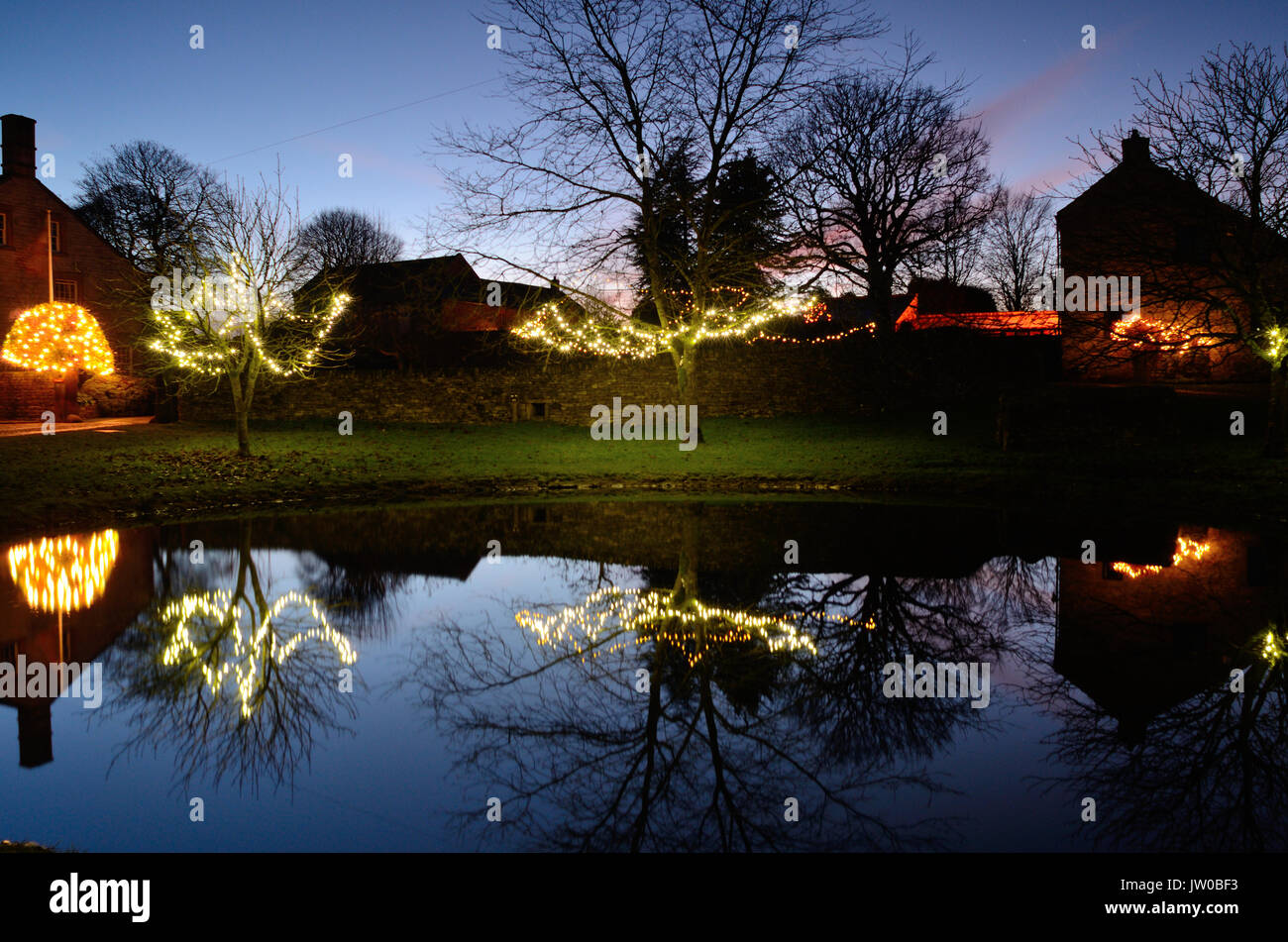 Le luci di Natale decorano alberi intorno al laghetto in Foolow, un pittoresco villaggio nel Peak District,Derbyshire,Inghilterra Regno Unito - Dicembre Foto Stock