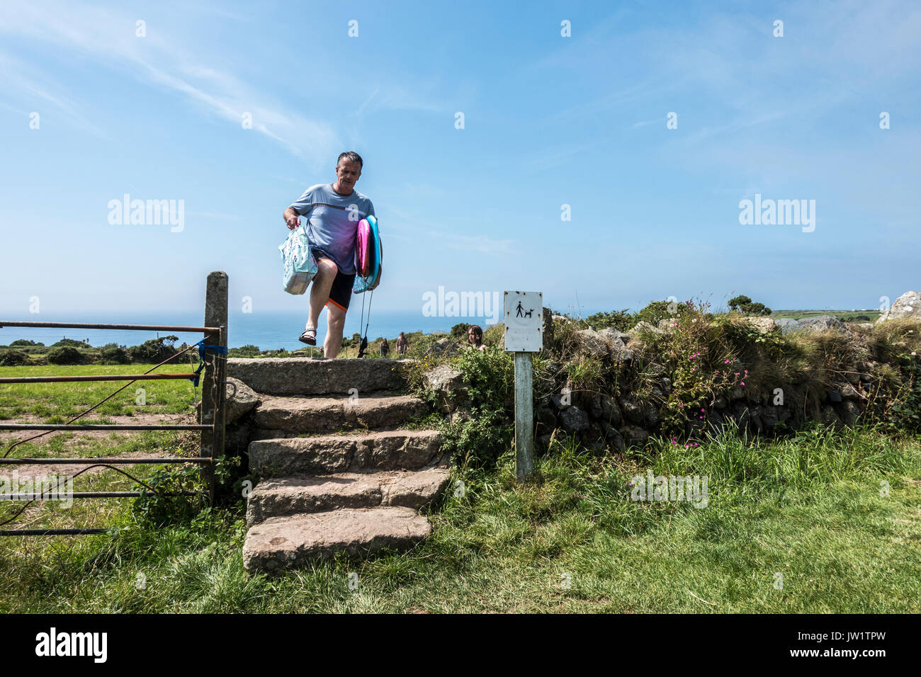 Un uomo che porta le tavole da surf durante la salita di gradini di pietra, dopo il ritorno dalla spiaggia Gwynver, Sennen, vicino a Penzance, Cornwall, Inghilterra, Regno Unito. Foto Stock