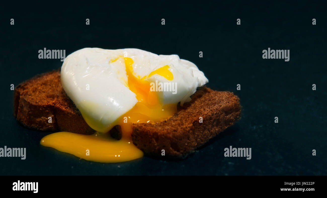 Uovo in camicia su una fetta di pane integrale. Foto su uno sfondo nero Foto Stock