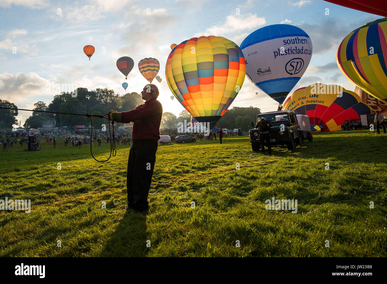 Un uomo mantiene la corona la linea regolare come mongolfiere decollare durante la prima salita di massa, dove mongolfiere provenienti da tutto il mondo si riuniranno a Ashton Court, Bristol, a prendere parte al Bristol International Balloon Fiesta. Foto Stock