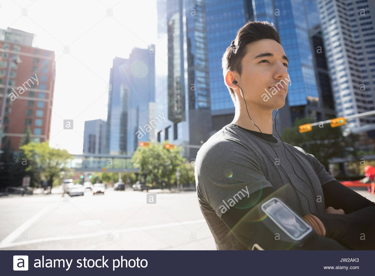 Ritratto fiducioso giovane maschio runner l'ascolto di musica con cuffie e lettore mp3 fascia braccio sulla soleggiata strada urbana Foto Stock