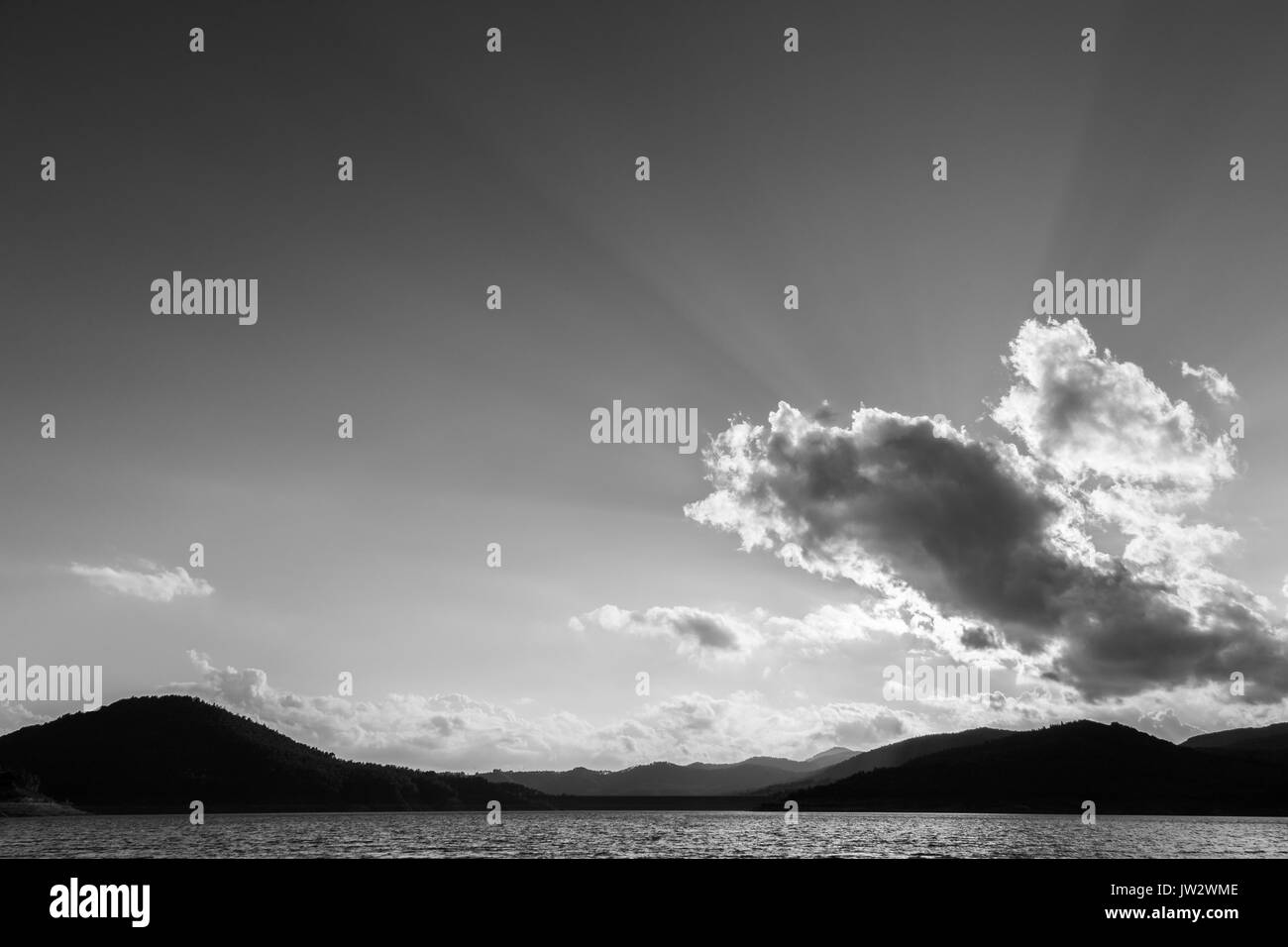 Potenti raggi del sole uscente attraverso alcune nuvole sopra un lago Foto Stock