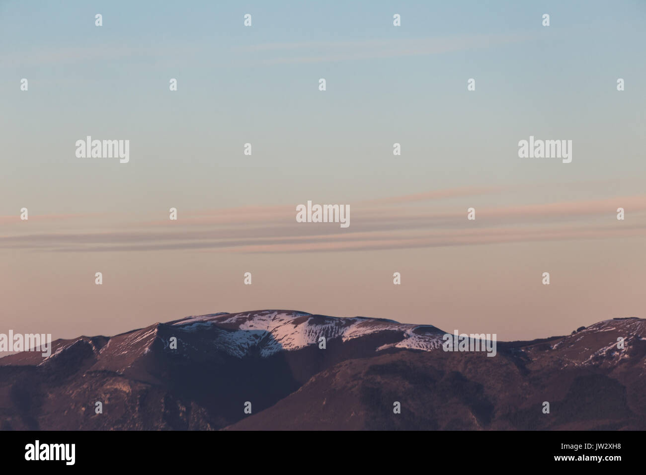 Un germoglio minimalista di alcune montagne top con neve, sotto un grande, quasi vuoto sky, con ora d'oro colori caldi e molto lunghe e sottili nuvole Foto Stock