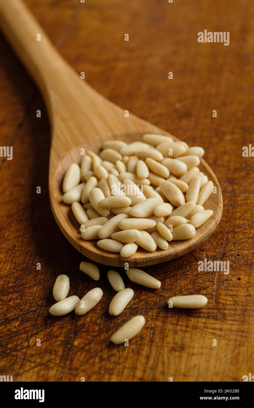 Cucchiaio di legno pieno di pinoli su tavola Foto Stock