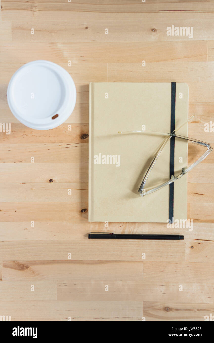 Tazza monouso, agenda, occhiali e penna sulla scrivania in legno Foto Stock