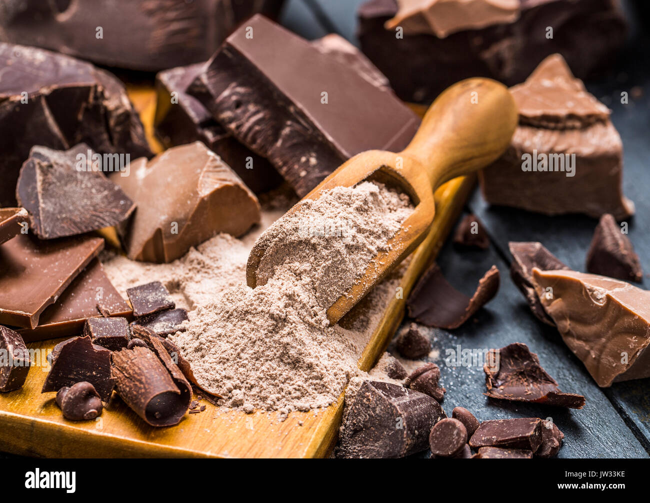 Vari pezzi di cioccolato attorno al cucchiaio di legno con cioccolato in polvere Foto Stock