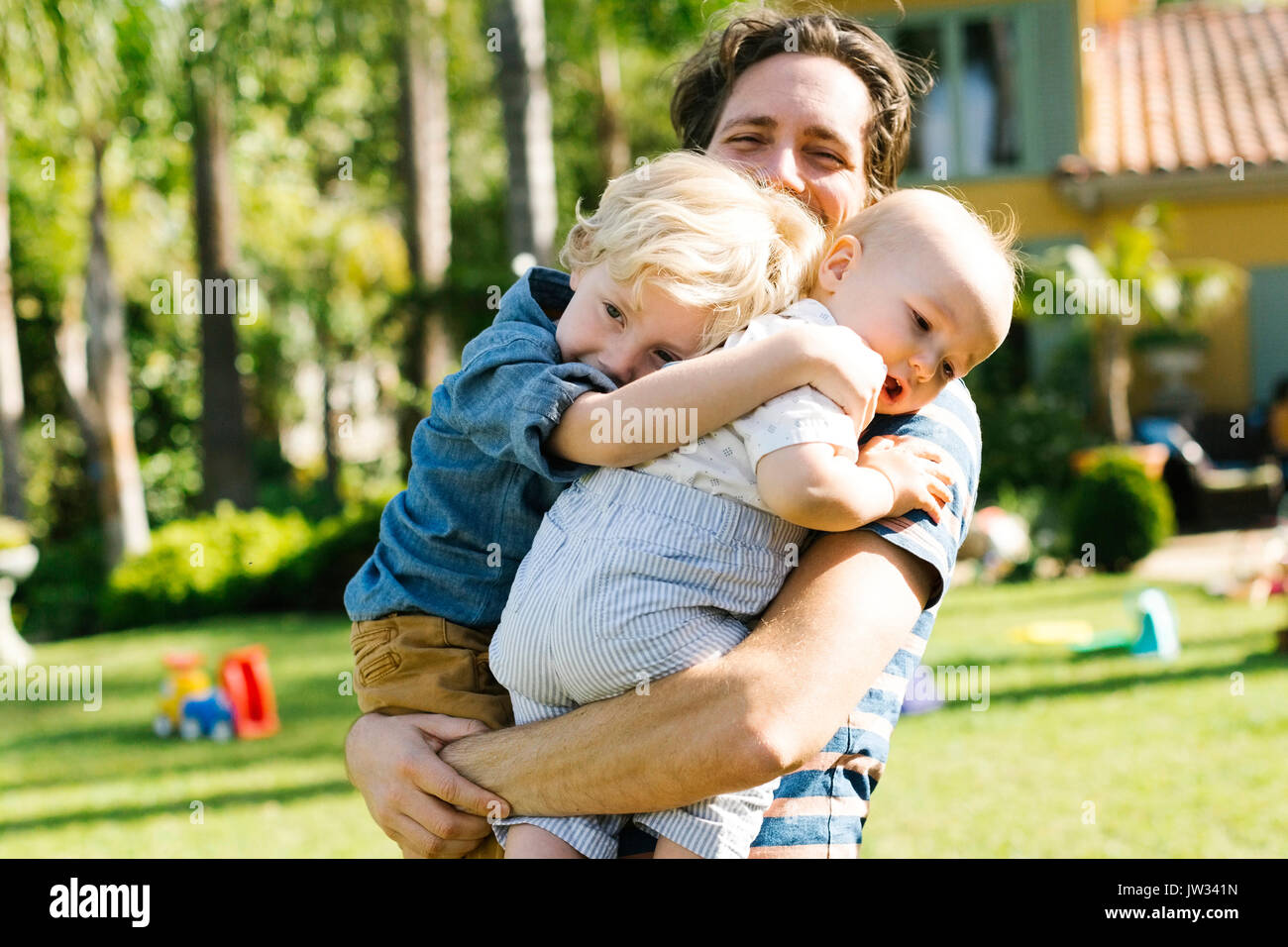 Padre con due figli (12-17 mesi, 4-5) giocando in cortile Foto Stock