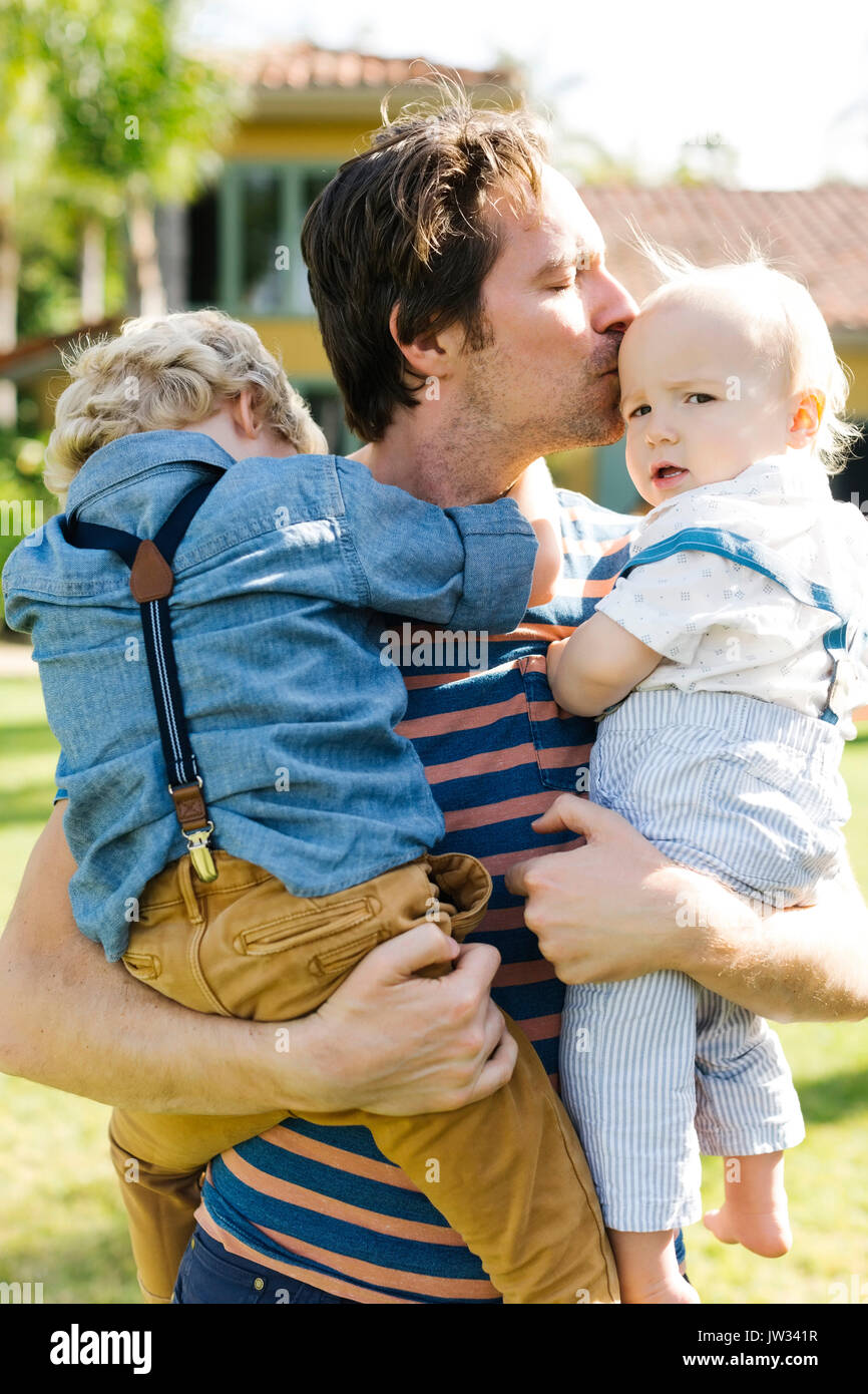 Padre con due figli (12-17 mesi, 4-5) giocando in cortile Foto Stock