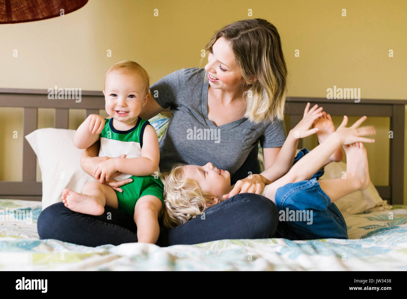 Madre con figli (12-17 mesi, 4-5) seduto sul letto Foto Stock