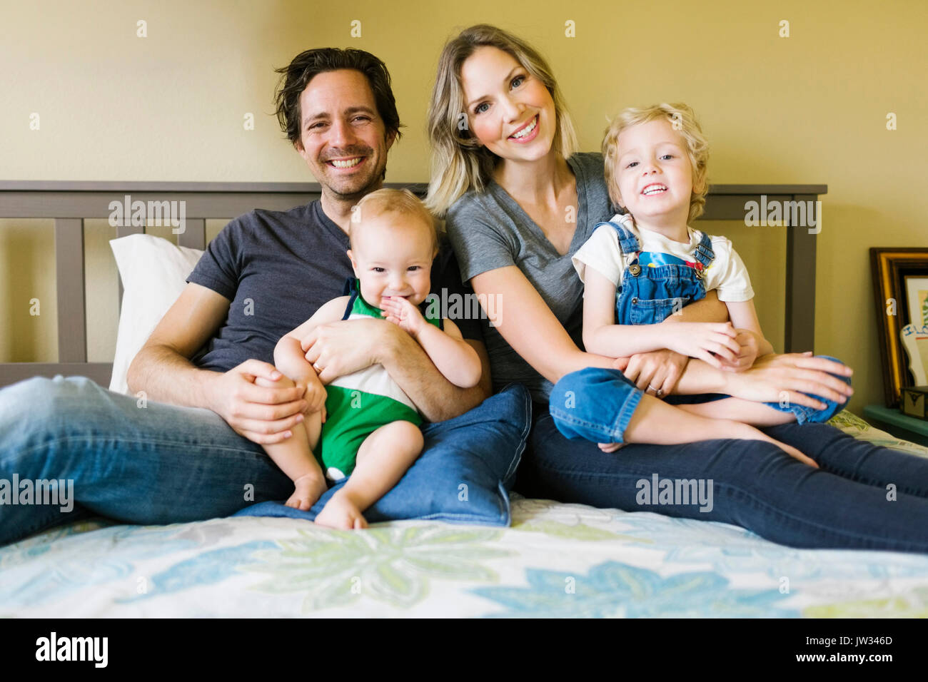 Ritratto di seduta i genitori con figli (12-17 mesi, 4-5) sul letto Foto Stock