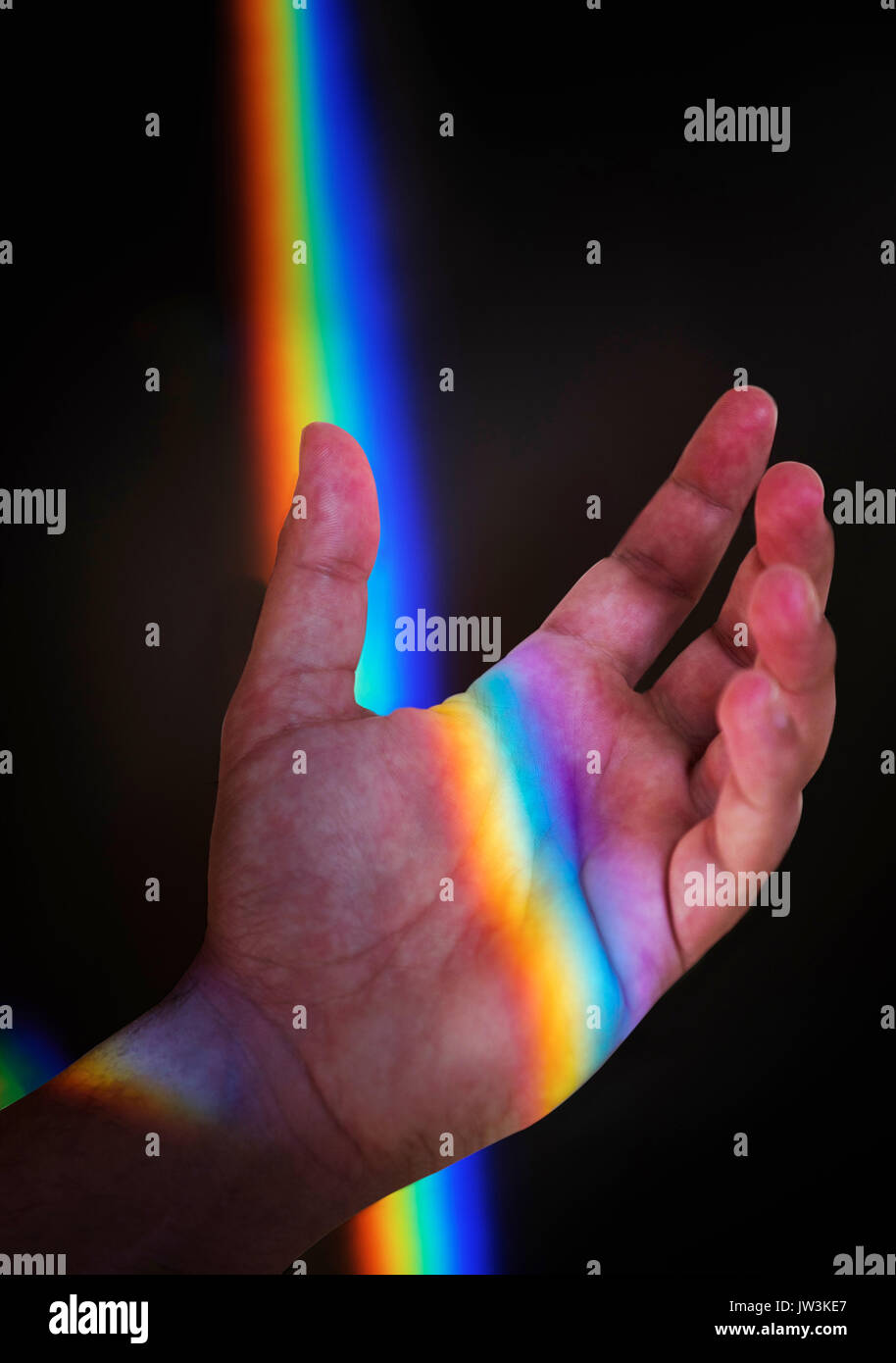 Mano d'uomo con luce arcobaleno contro il nero Foto Stock