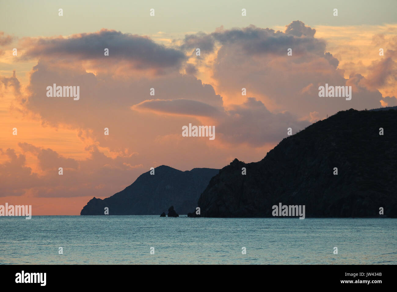 Spettacolare mare di Cortez scena costiera con scogliere nere immergersi in acque turchesi mentre la fuga di nuvole riempire l'arancione/rosa cielo sopra. Foto Stock
