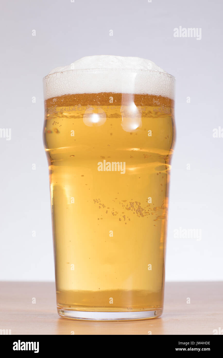Un spillata di fresco e spumosi pinta di birra su una tavola di legno al top con sfondo bianco e copiare lo spazio verticale in orientamento verticale. Foto Stock