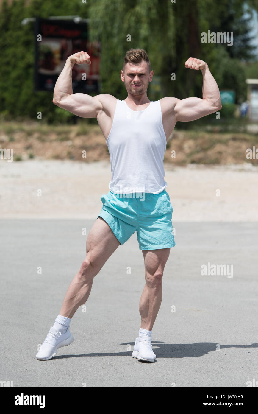 Bel giovane uomo forte permanente all'aperto e flettendo i muscoli - Atletico muscolare Bodybuilder Modello di Fitness in posa dopo esercizi Foto Stock