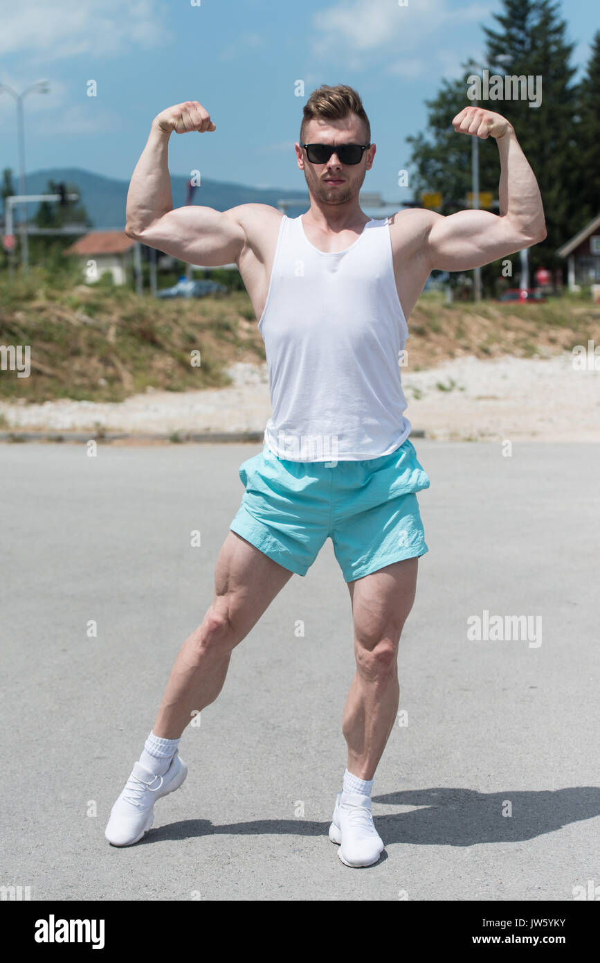 Sano giovane uomo forte all'aperto e flettendo i muscoli - Atletico muscolare Bodybuilder Modello di Fitness in posa dopo esercizi Foto Stock
