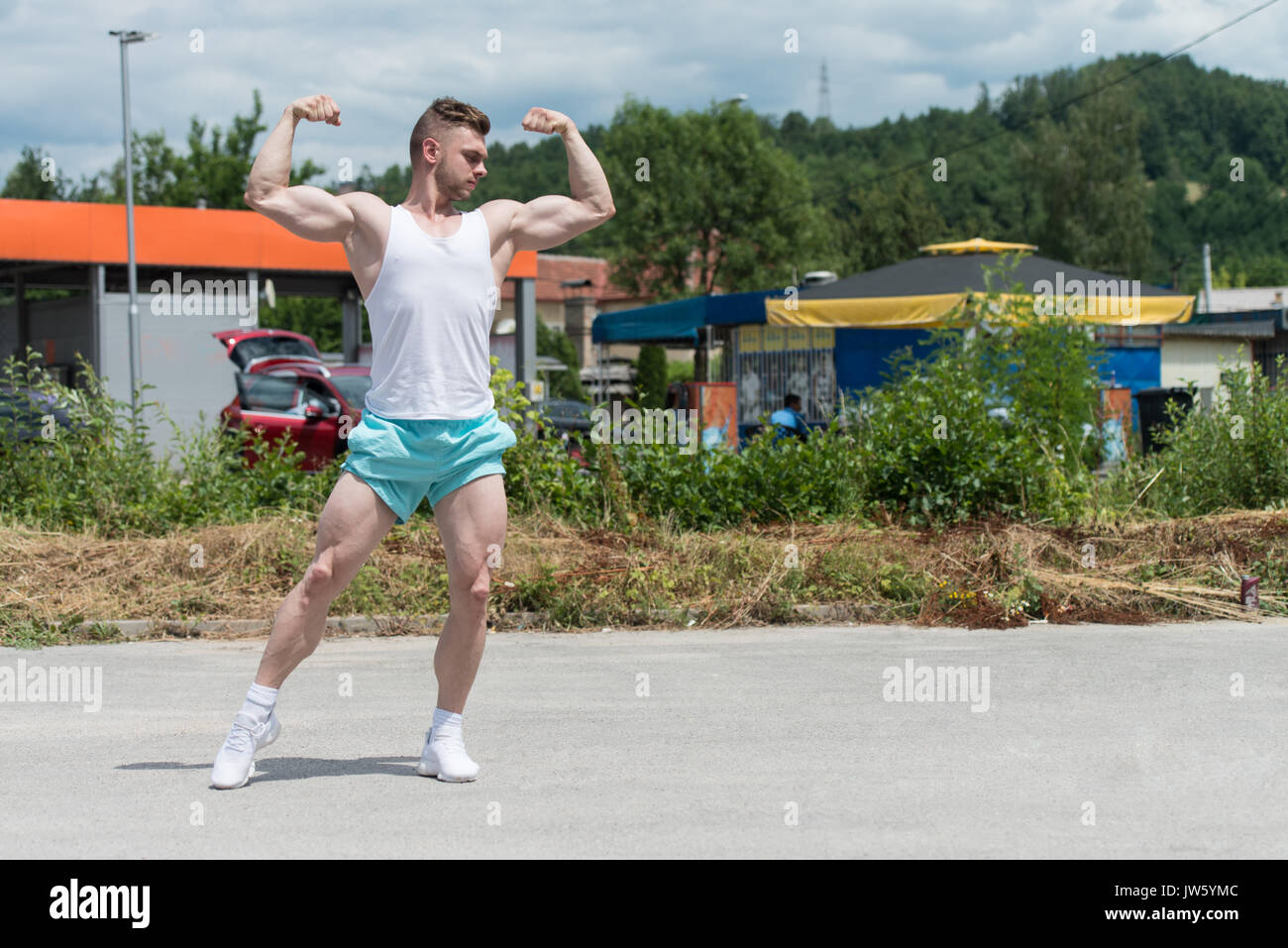 Bel giovane uomo forte permanente all'aperto e flettendo i muscoli - Atletico muscolare Bodybuilder Modello di Fitness in posa dopo esercizi Foto Stock