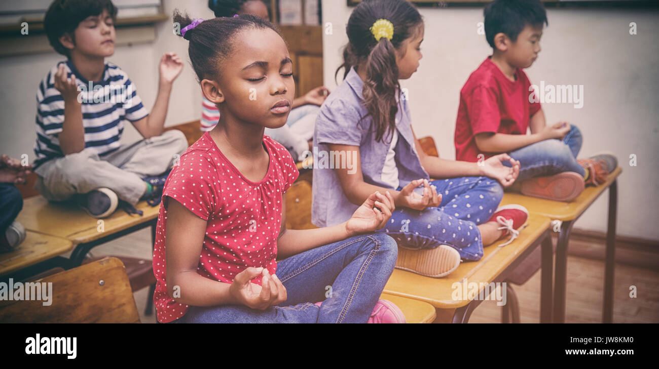 Gli alunni meditando nella posizione del loto sulla scrivania in aula presso la scuola elementare Foto Stock