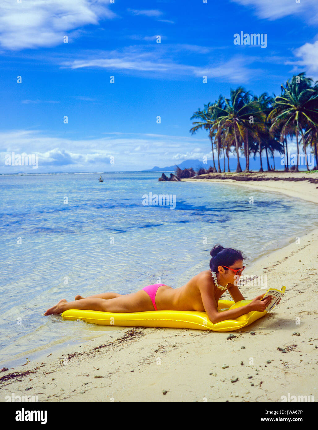 Giovane donna in topless che prende il sole sul materasso ad aria gialla del  letto, leggendo un libro, spiaggia tropicale, palme, mare caraibico,  Guadalupa, Antille francesi, piccole Antille Foto stock - Alamy