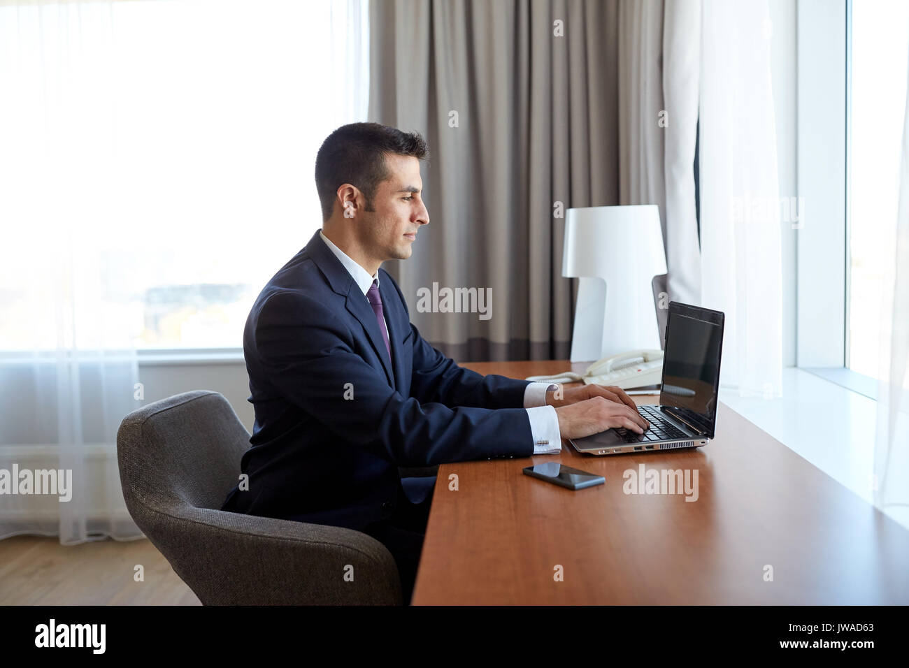 Imprenditore digitando su laptop in camera di albergo Foto Stock