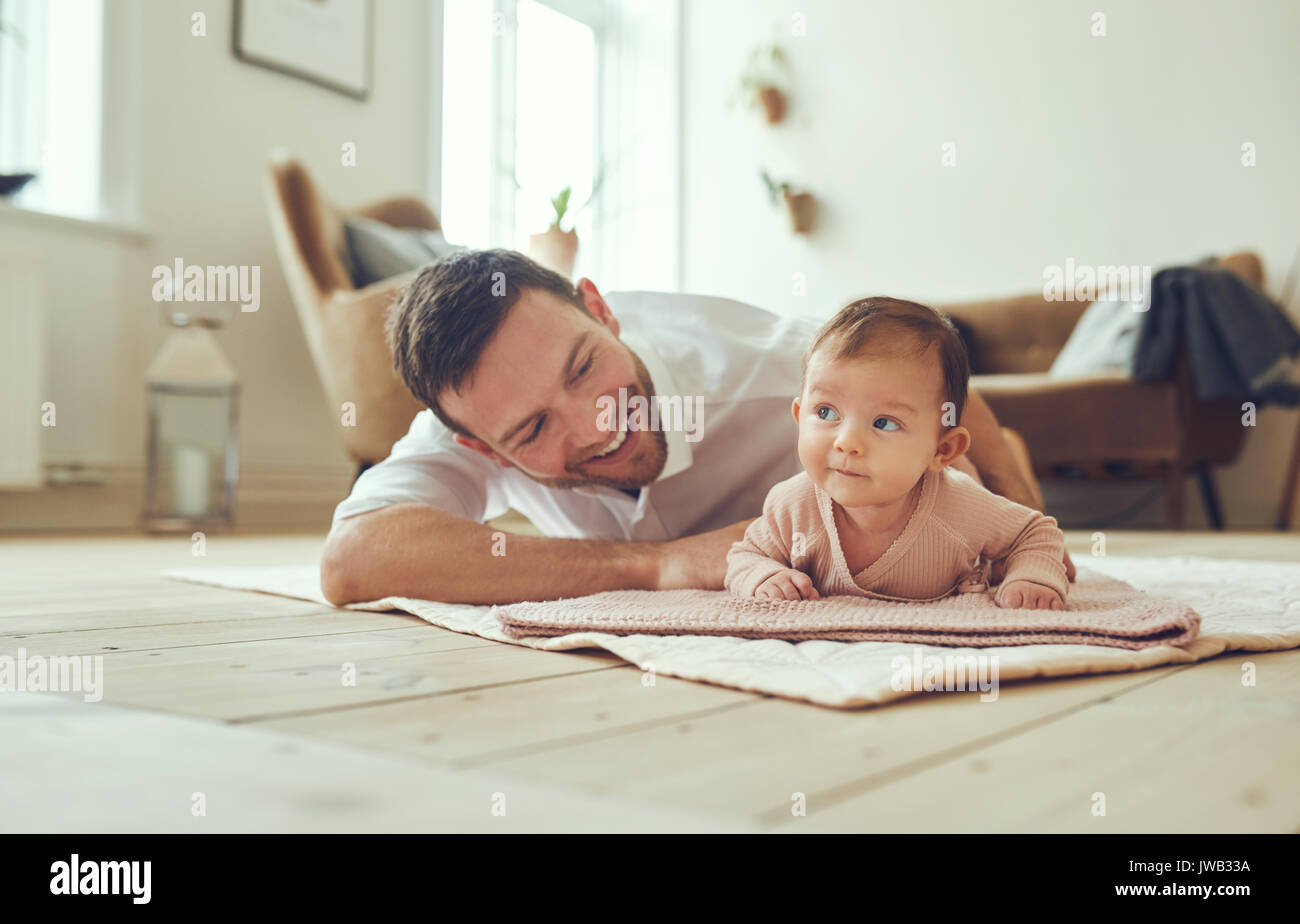 Sorridente giovane padre giacente su coperte sul al piano salotto di casa con la sua adorabile figlia bambino Foto Stock