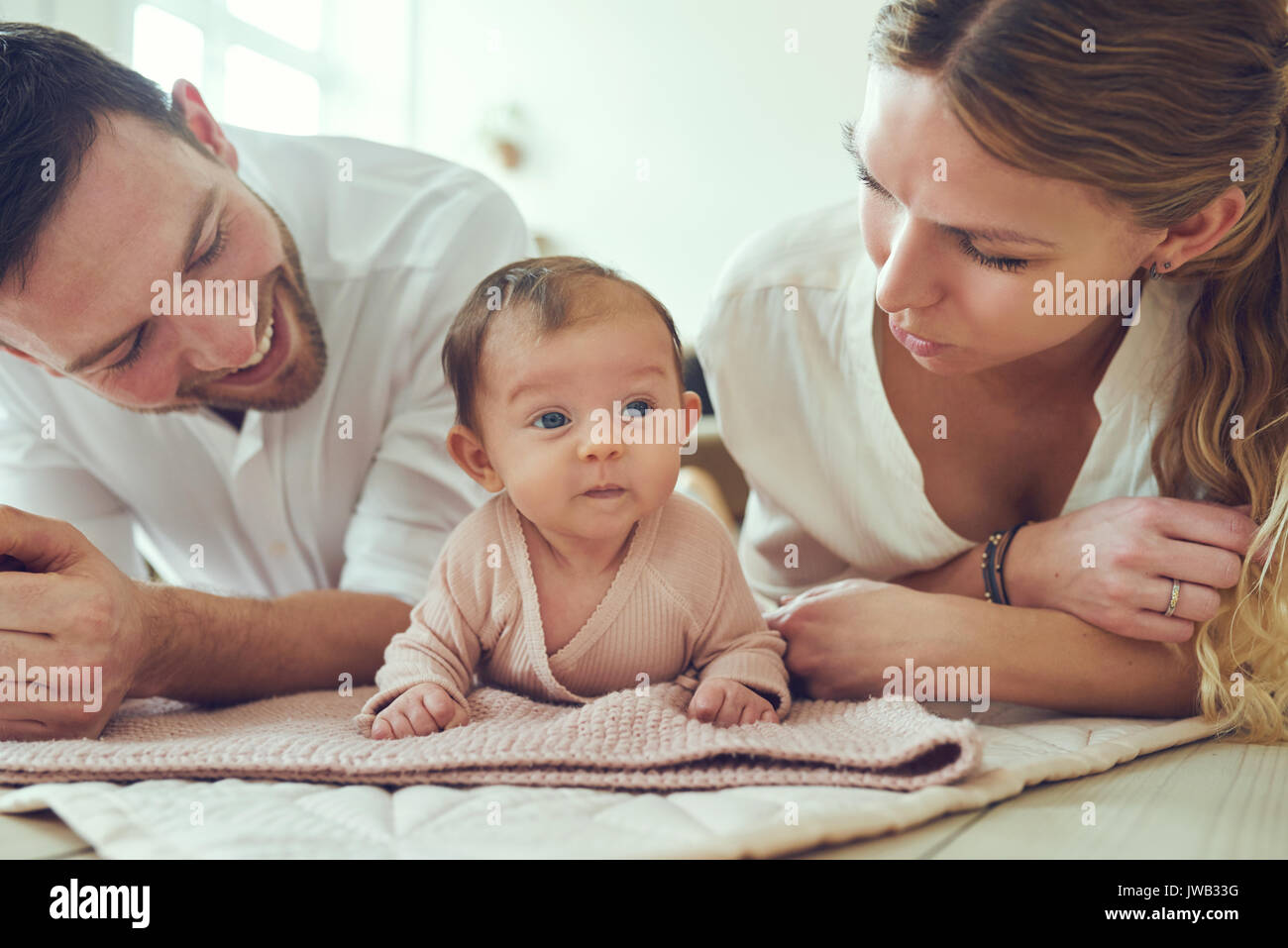 Sorridente giovane madre e padre giacente su coperte sul loro soggiorno piano a casa con il loro adorabile figlia bambino Foto Stock