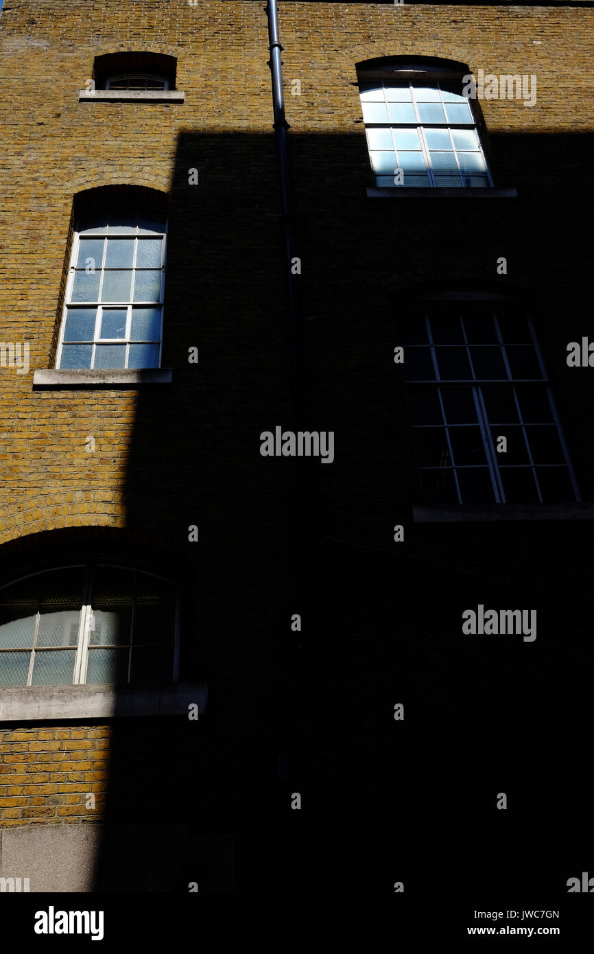 Come il sole tramonta, una lunga ombra viene colato su un molo vecchio edificio sulla riva sud del Tamigi a Londra Foto Stock