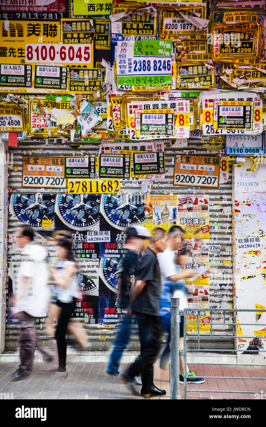 HONG KONG - Luglio 10, 2017: poster, volantini e pubblicità riempire ogni centimetro di una parete nel trafficato centro cittadino di quartiere di Mong Kok come pedoni hurri Foto Stock