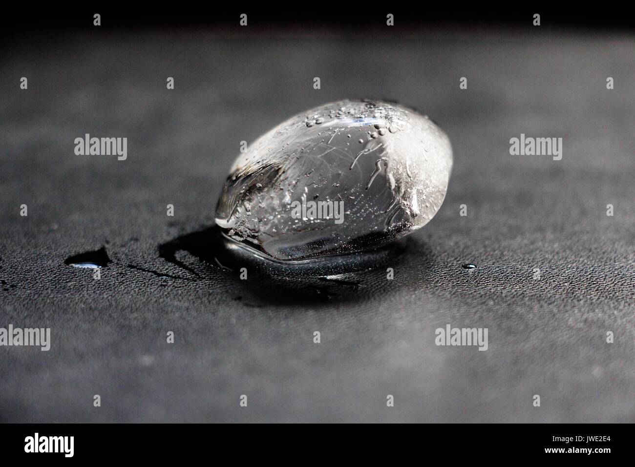 Un pezzo di ghiaccio che appena ha cominciato a fondere giace su una superficie nera. Foto Stock