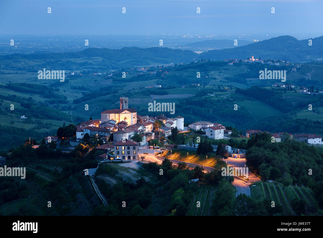 Medieval hilltop village di Brda Smartno Slovenia al crepuscolo e nelle colline di Gorizia con la chiesa di San Martino, Medana villaggio italiano e le luci della città in Foto Stock