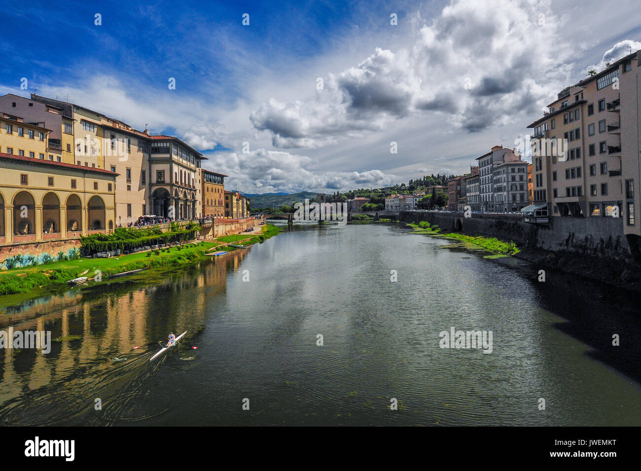 Un singolo scull si muove lungo il fiume Arno sotto una drammatica estate cielo Foto Stock